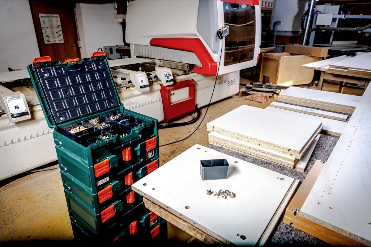 Nowoczesny zakład obróbki drewna. Na pierwszym planie leży zielona skrzynka narzędziowa. Różne deski drewniane na stole warsztatowym.