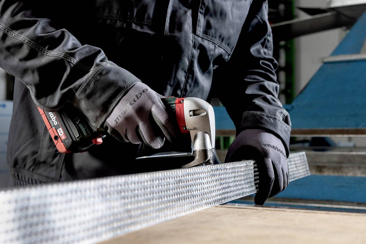 Osoba używa elektronarzędzia do cięcia metalu. Otoczenie wskazuje na warsztat lub środowisko przemysłowe.