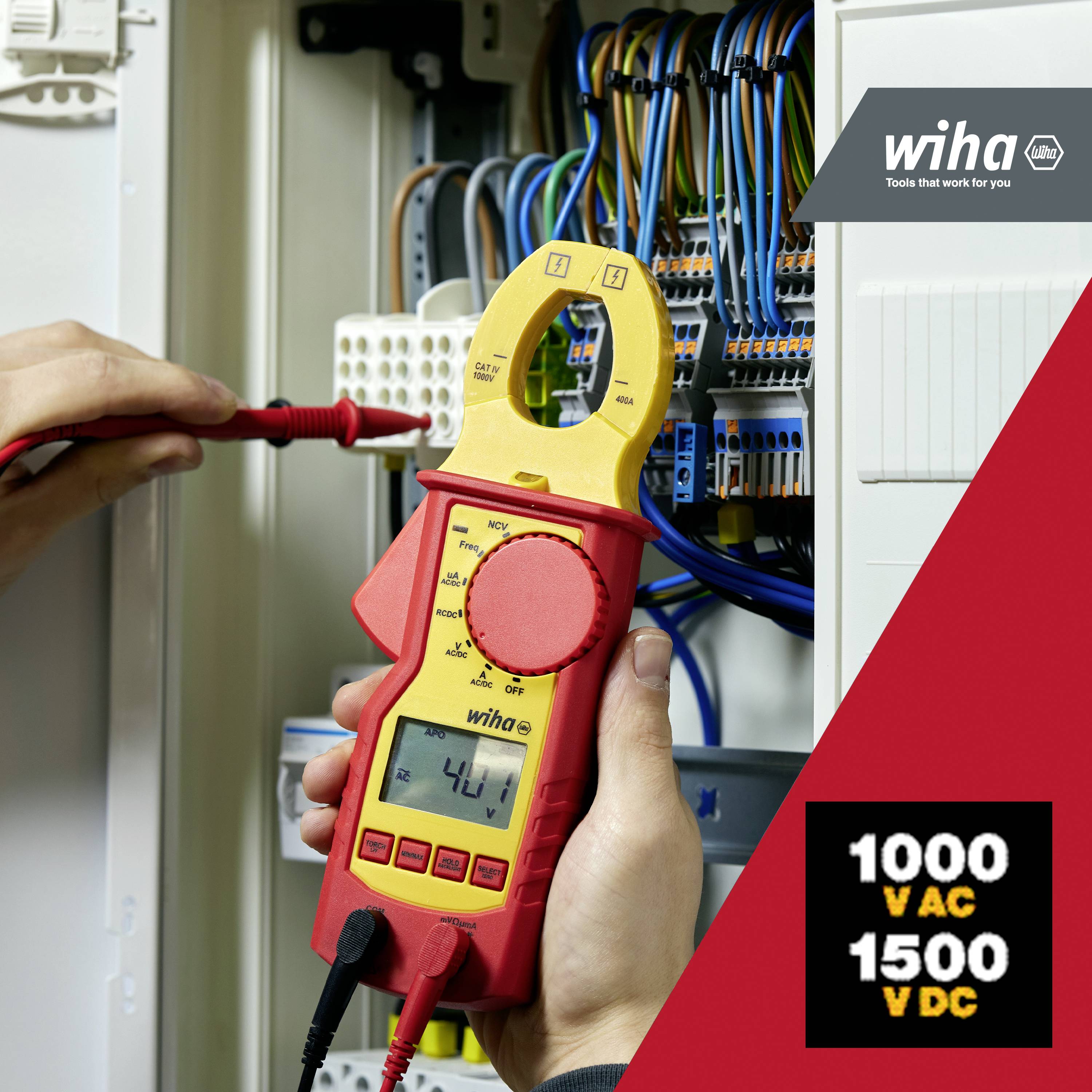 Osoba trzyma miernik napięcia podczas sprawdzania rozdzielnicy elektrycznej. Urządzenie wyświetla wartość '41,1'. W tle widoczny jest układ elektryczny.