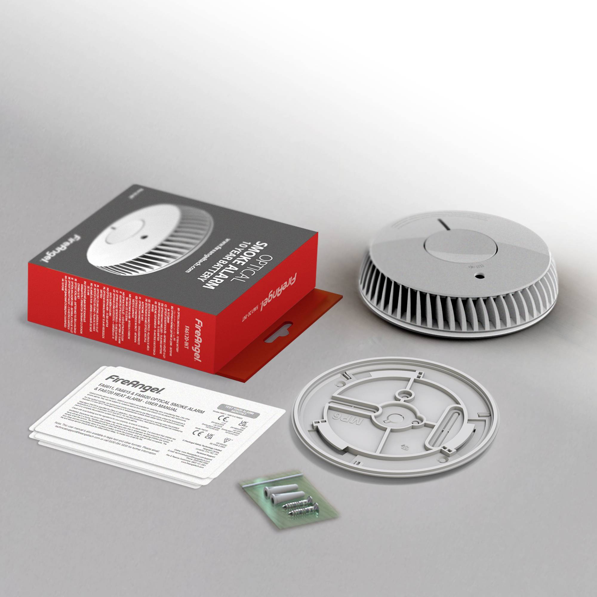 Czujnik dymu z akcesoriami: opakowanie, baterie, płytka montażowa i instrukcja obsługi rozłożone są na stole.