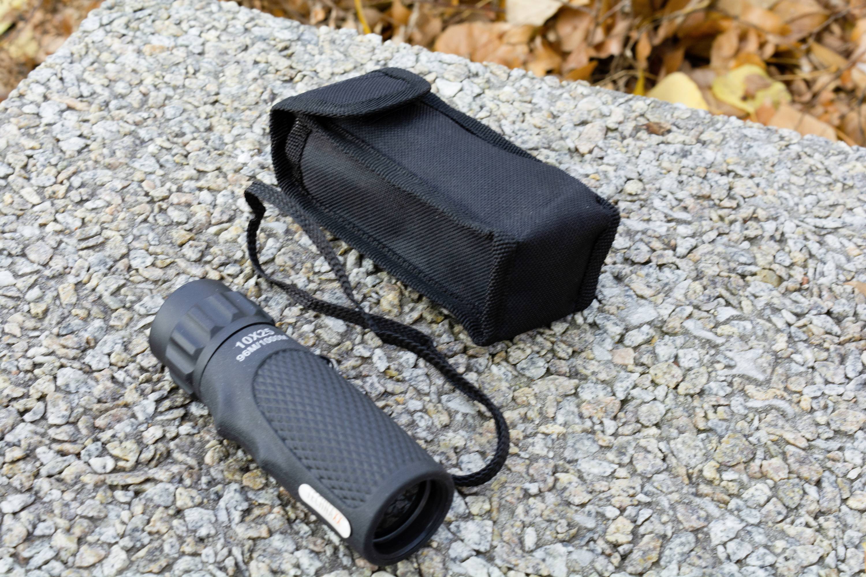 Latarka i czarne etui na kamieniu z jesiennymi liśćmi w tle.