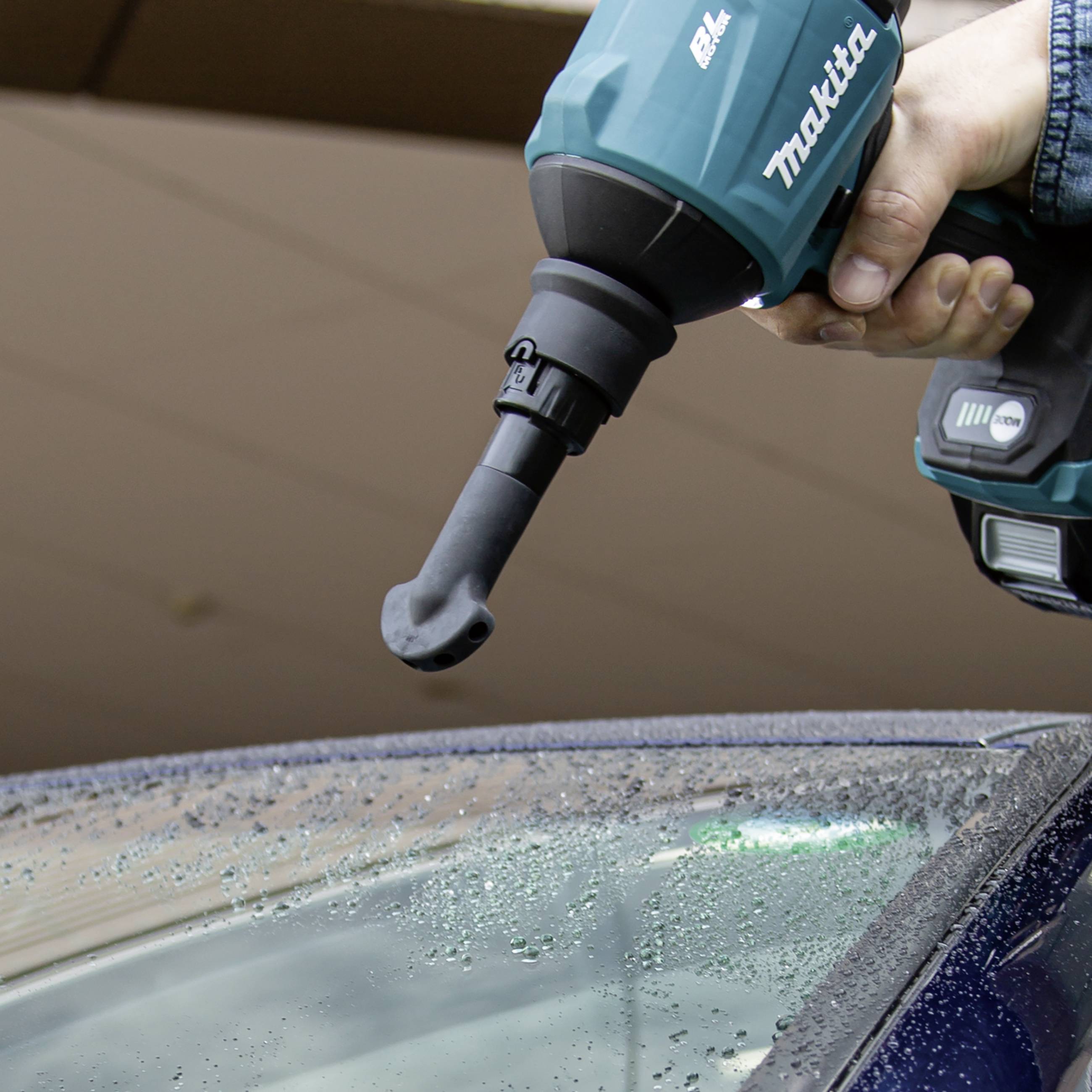 Osoba trzyma bezprzewodowe elektronarzędzie z końcówką szczotkową nad mokrym dachem samochodu, przygotowując się do jego czyszczenia.