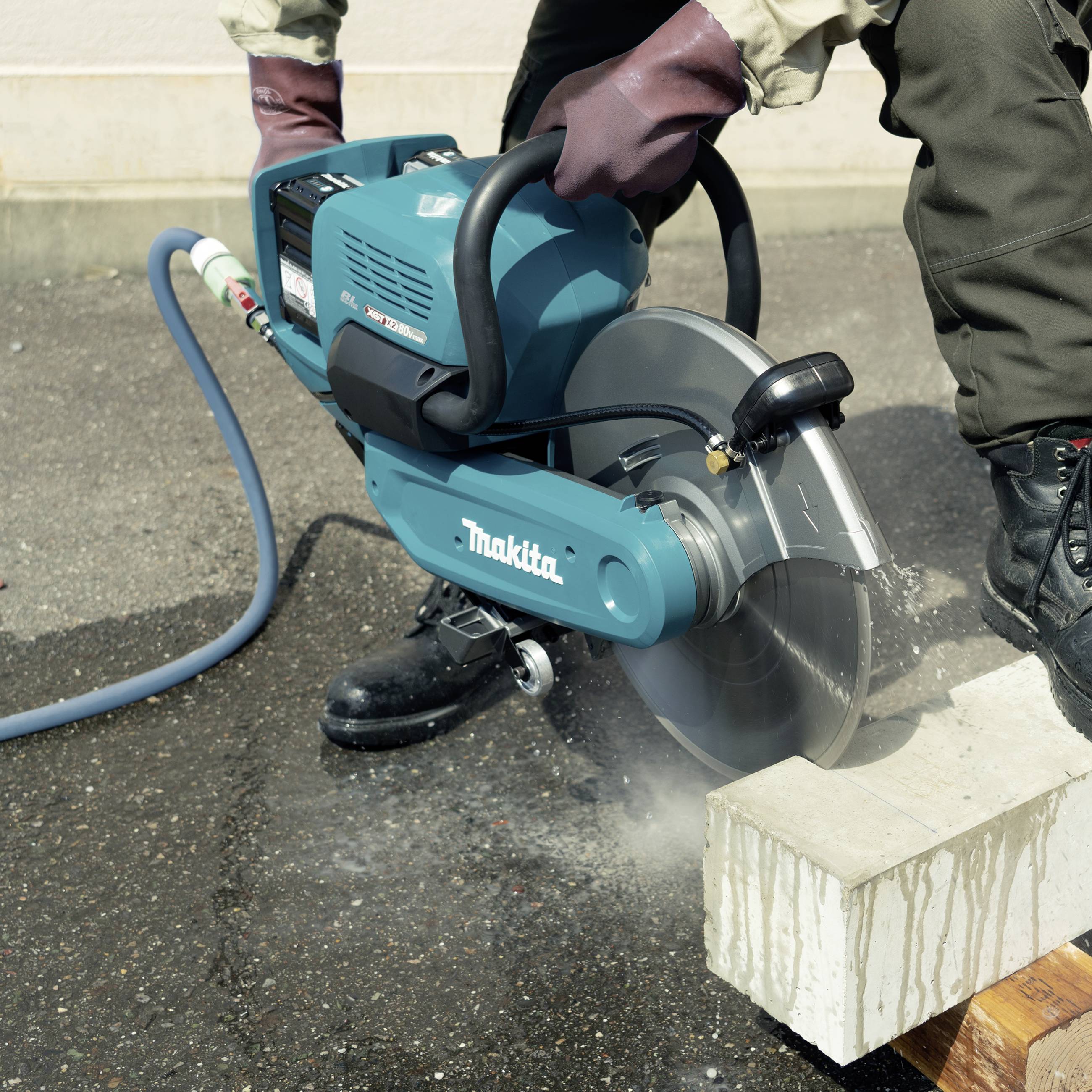 Osoba tnie betonowy kamień zmotoryzowaną piłą na asfalcie, nosząc rękawice i odzież ochronną.