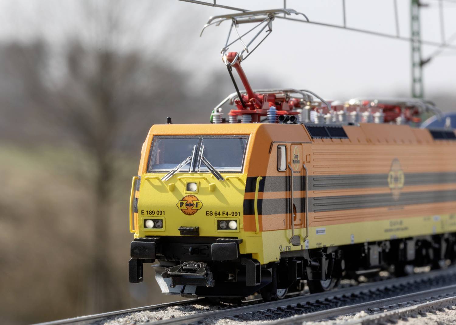 Żółto-pomarańczowy pociąg jedzie po torach, otoczony rozmytym krajobrazem w tle. Pociąg posiada logo 'PKP Cargo'.