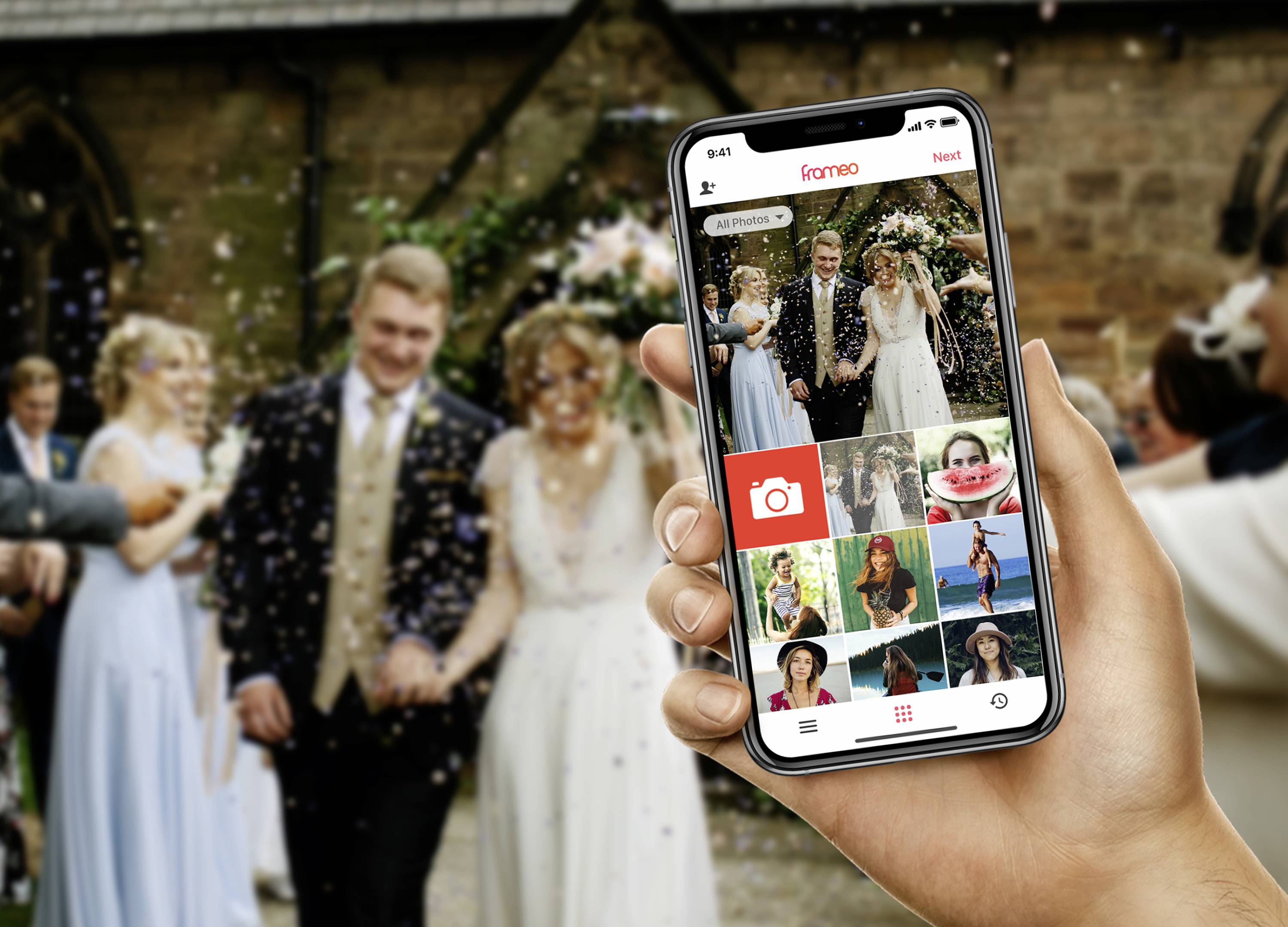 Osoba trzyma smartfon z aplikacją fotograficzną, w tle para młoda i goście weselni.