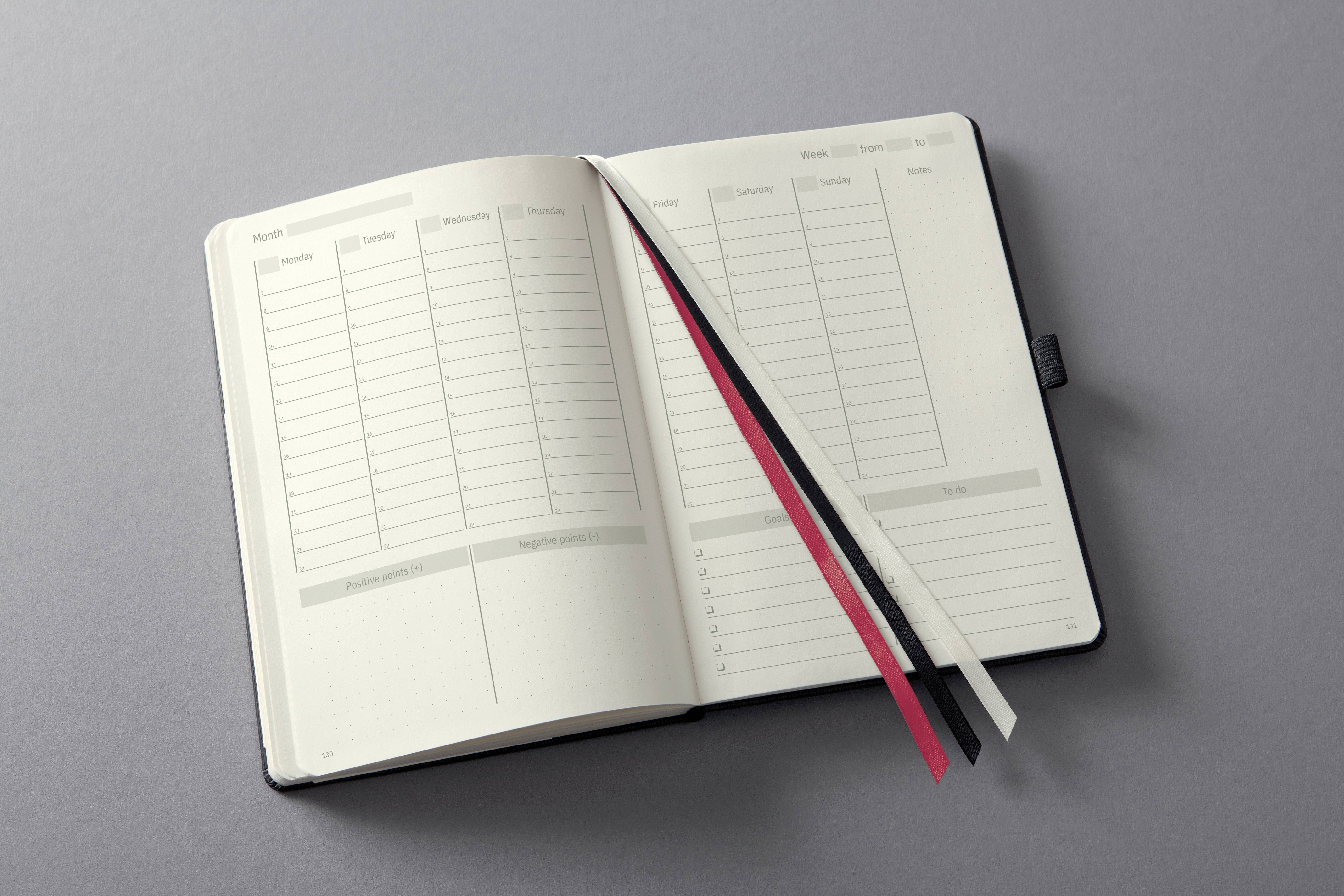 Otwarty planer z przeglądem tygodnia po lewej stronie i przestrzenią na notatki po prawej. Trzy zakładki w kolorach czerwonym, czarnym i białym leżą na nim.