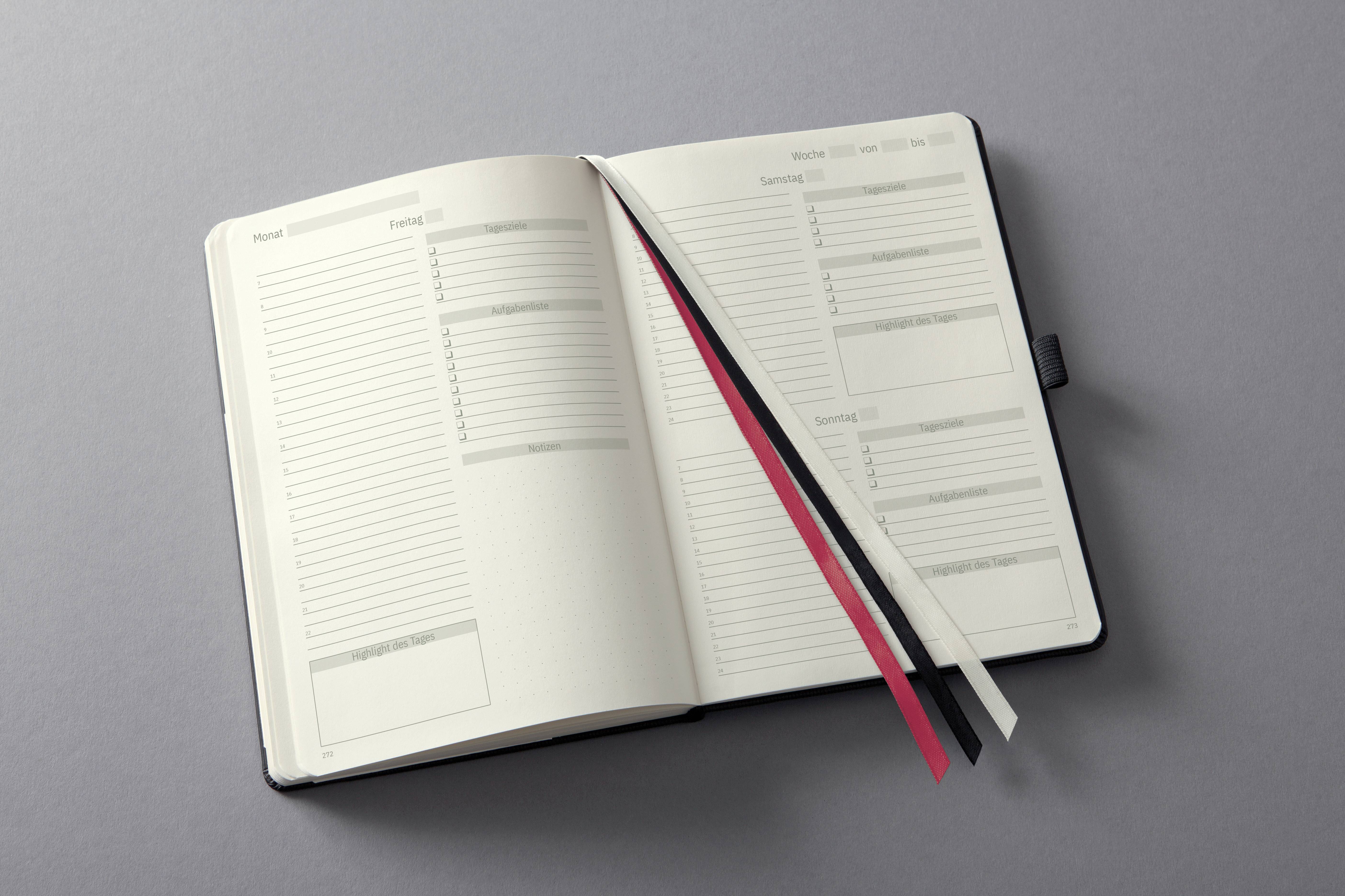 Otwarty planer na szarym tle prezentuje puste strony z miejscem na planowanie tygodnia i notatki; trzy zakładki w kolorach czerwonym, czarnym i białym.