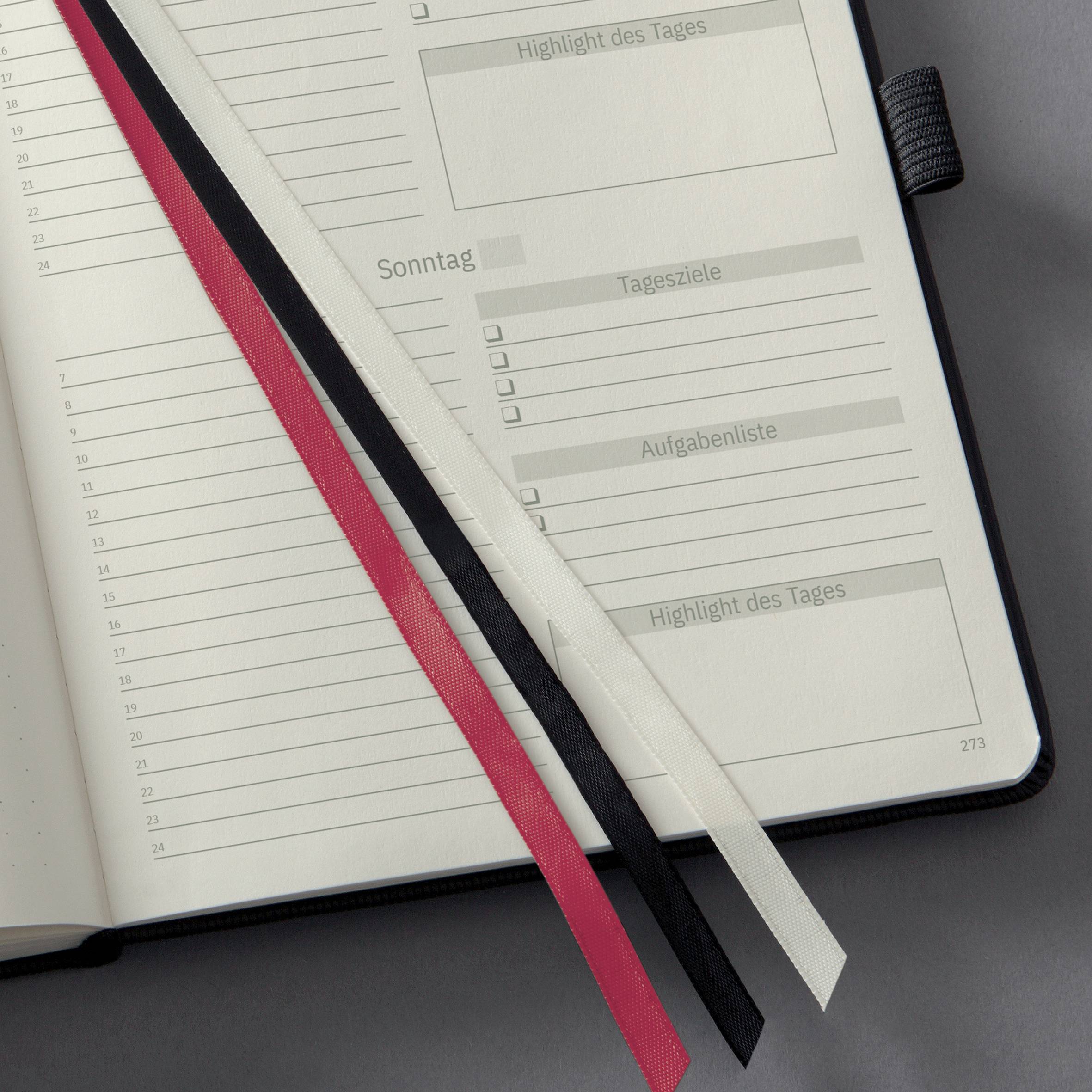 Planer z otwartymi stronami. Linie do notatek, kategorie takie jak 'Highlight dnia', 'Cele dnia'. Zakładki w kolorach czerwonym, czarnym, białym.