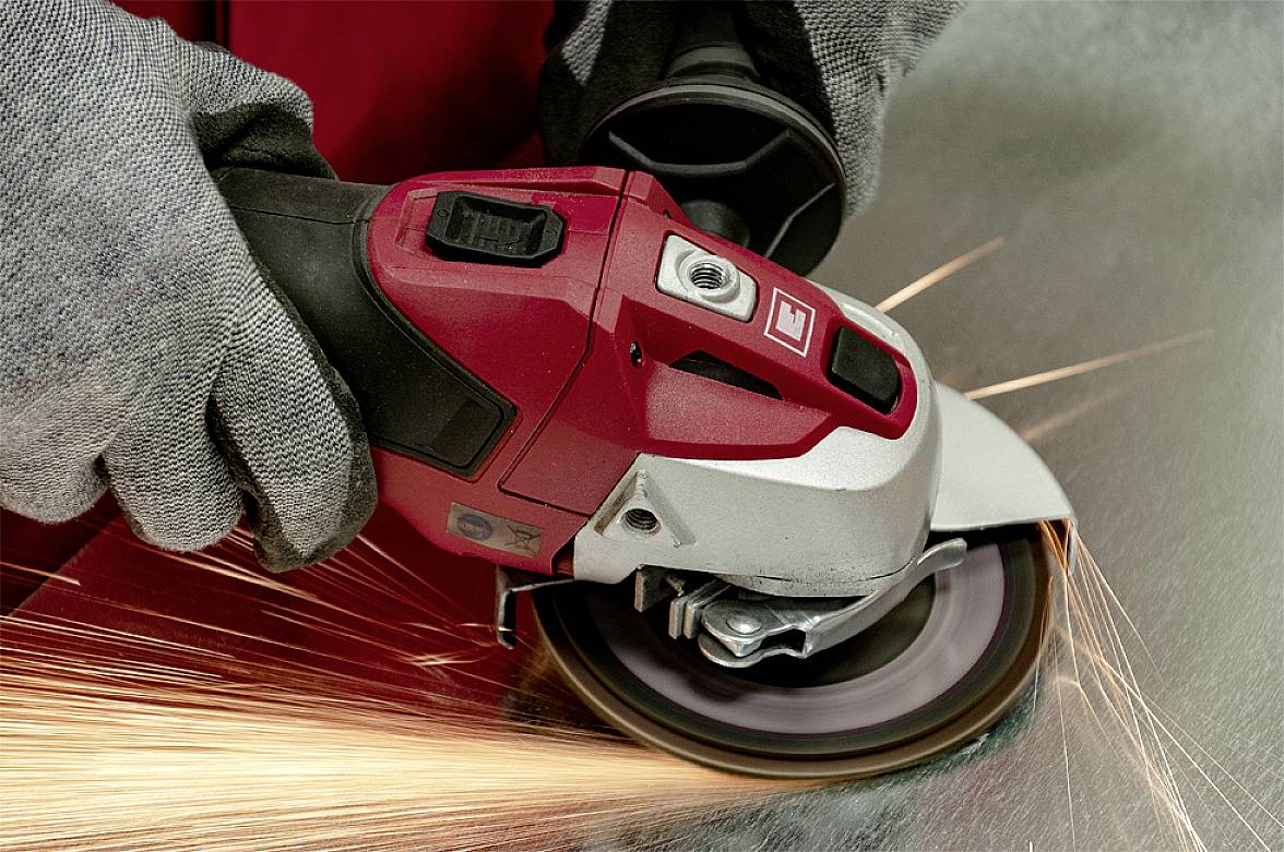 Osoba szlifuje powierzchnię metalową szlifierką kątową. W punkcie kontaktu tryskają iskry.