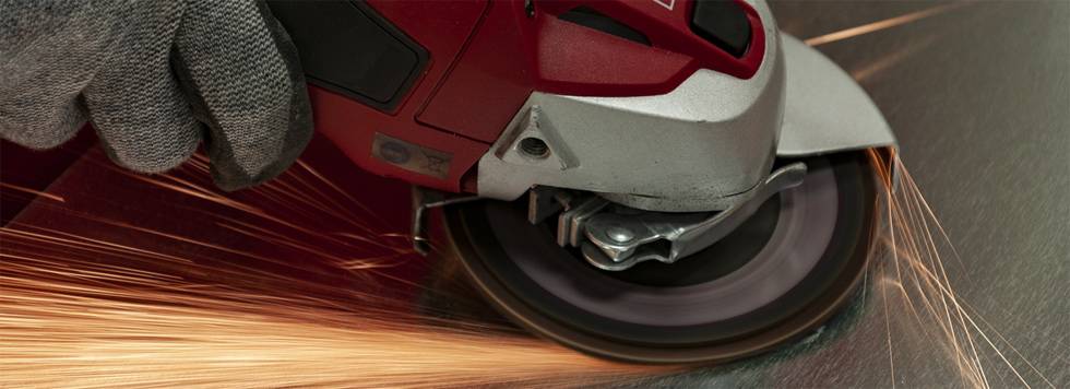 Osoba szlifuje blachę metalową szlifierką kątową. Iskry lecą od tarczy.