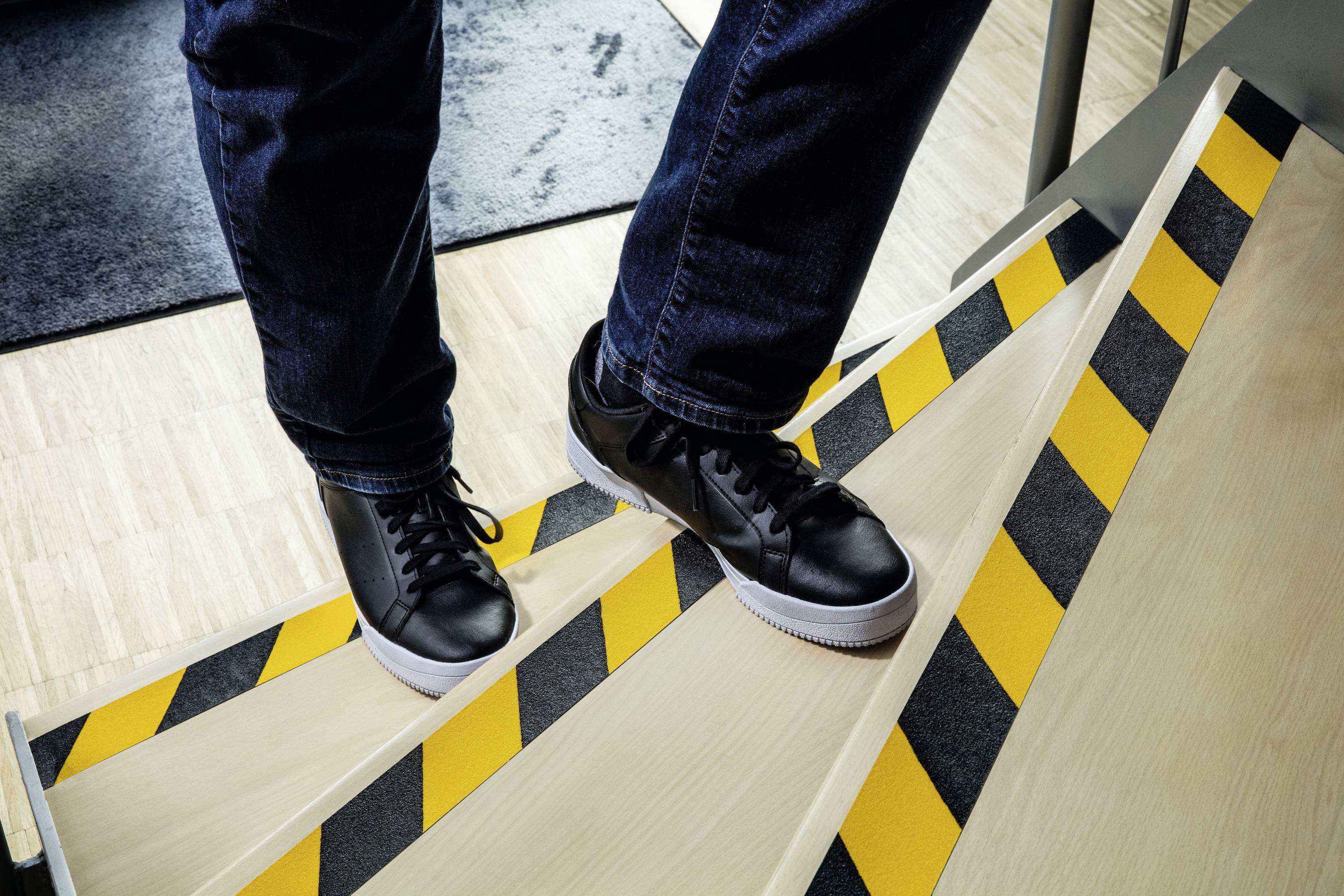 Osoba schodzi po schodach z żółto-czarnymi pasami ostrzegawczymi w tenisówkach.