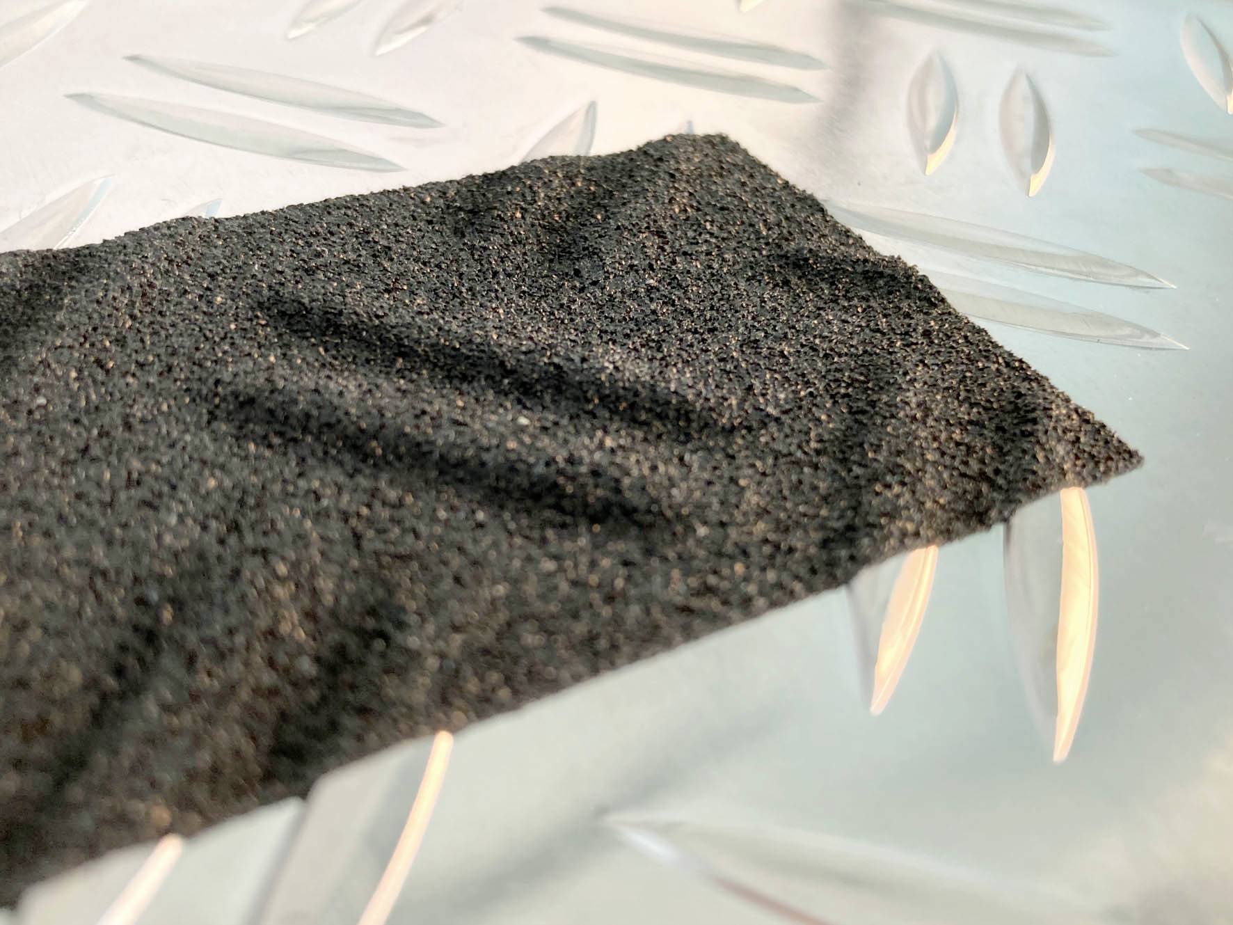 Czarny kawałek papieru ściernego leży na srebrnej metalowej płycie z wzorem rombu.