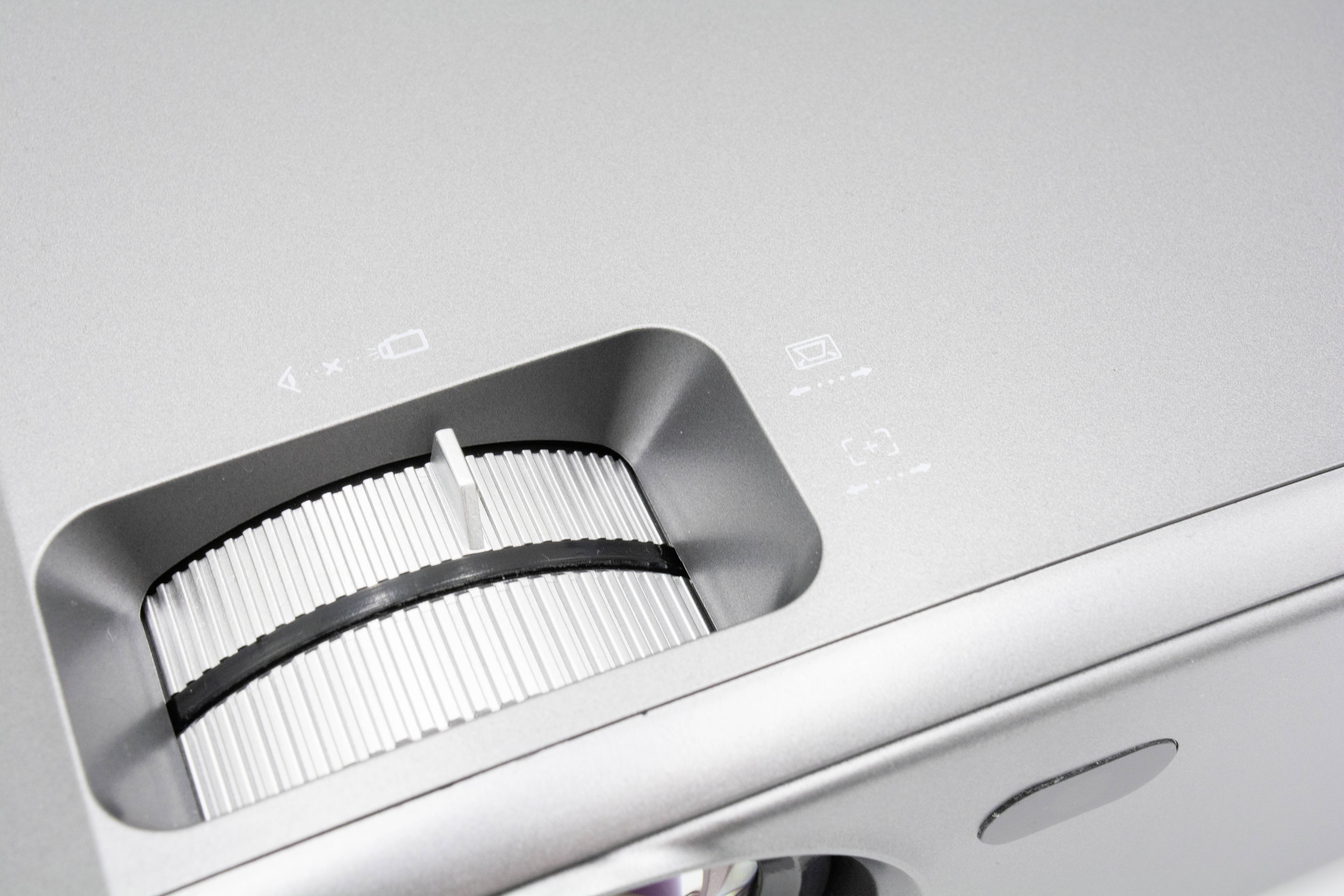 Srebrny projektor z pierścieniem ostrości i panelem sterowania.