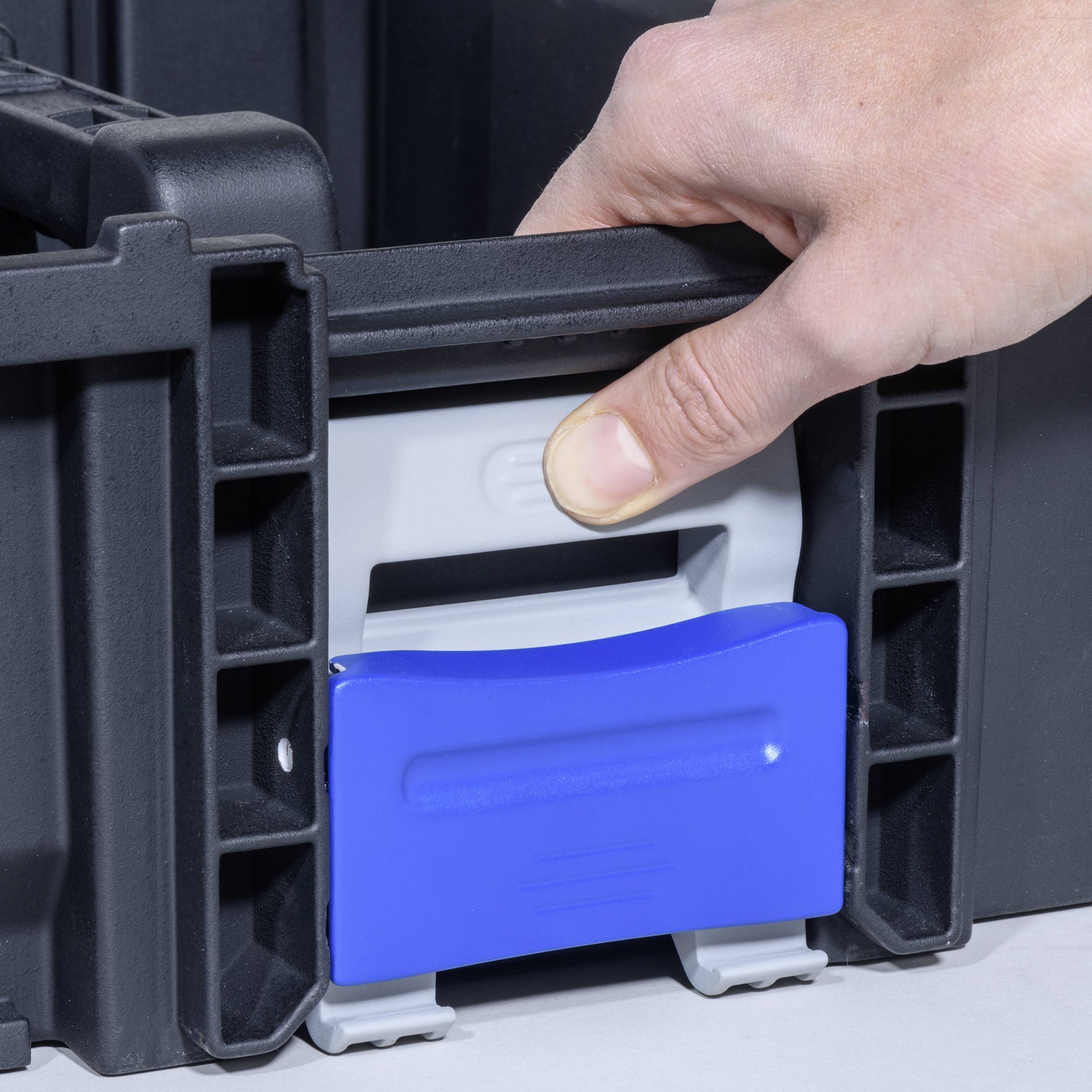 Jedna ręka wyciąga niebieką szufladę z czarnej obudowy z tworzywa sztucznego.