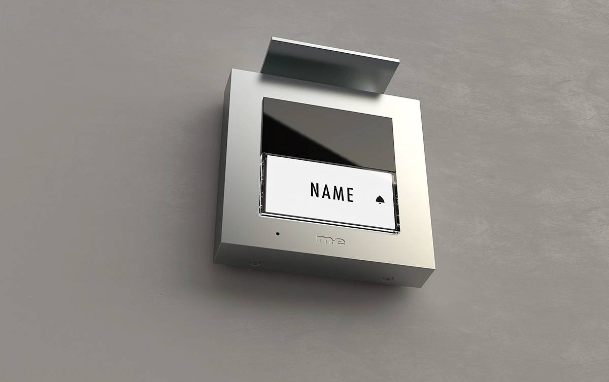 Srebrny domofon z ekranem i polem na tabliczkę z napisem 'Nazwisko'. Powierzchnia urządzenia ma nowoczesny design.