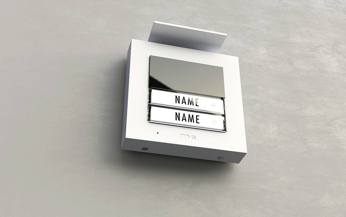 Tabliczka dzwonkowa z dwoma polami na nazwiska, zamontowana na ścianie, pusta, o błyszczącej, refleksyjnej powierzchni i nowoczesnym designie.
