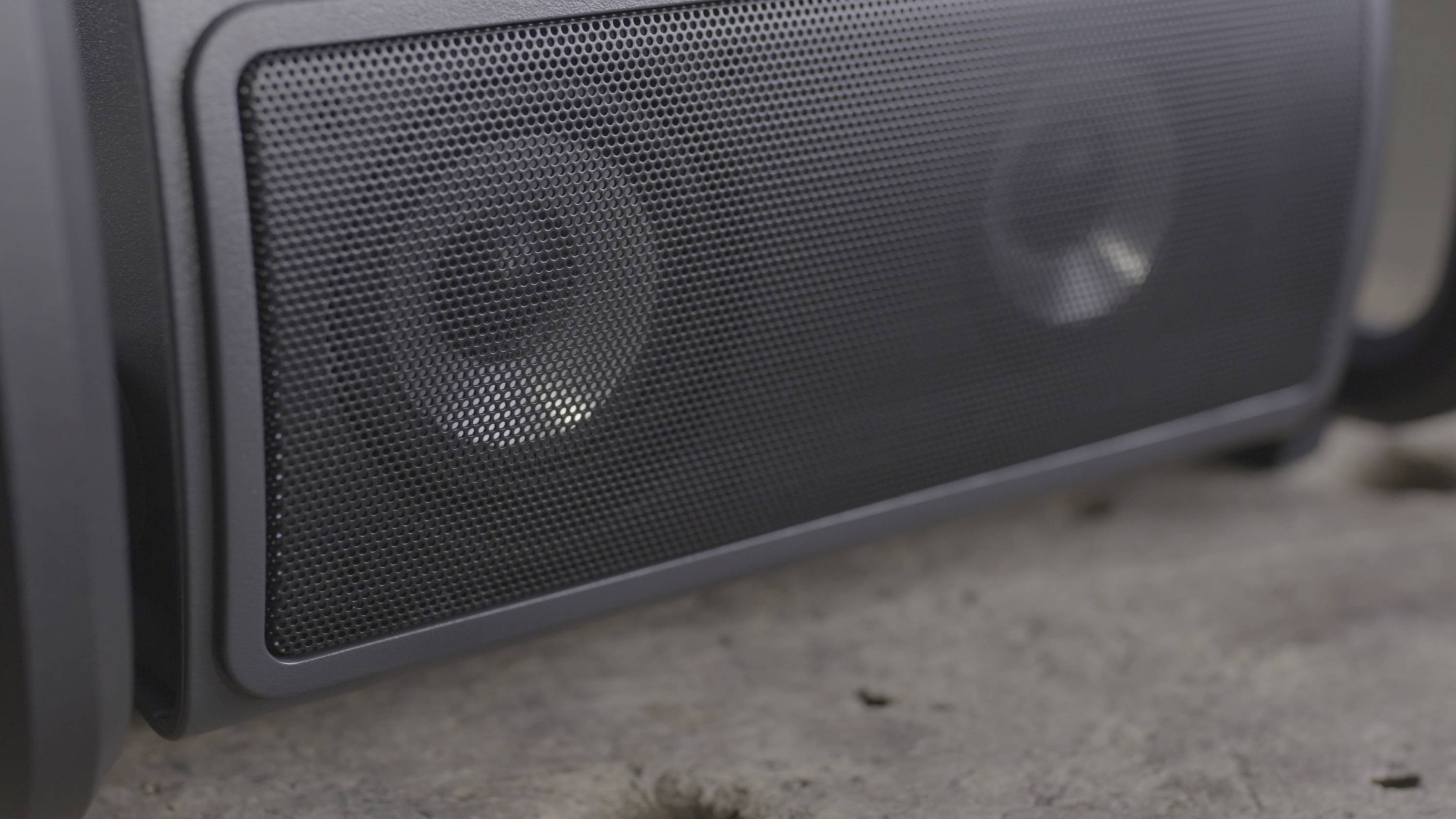Zbliżenie czarnego, przenośnego głośnika z metalową siatką. Głośnik stoi na betonowej podłodze.