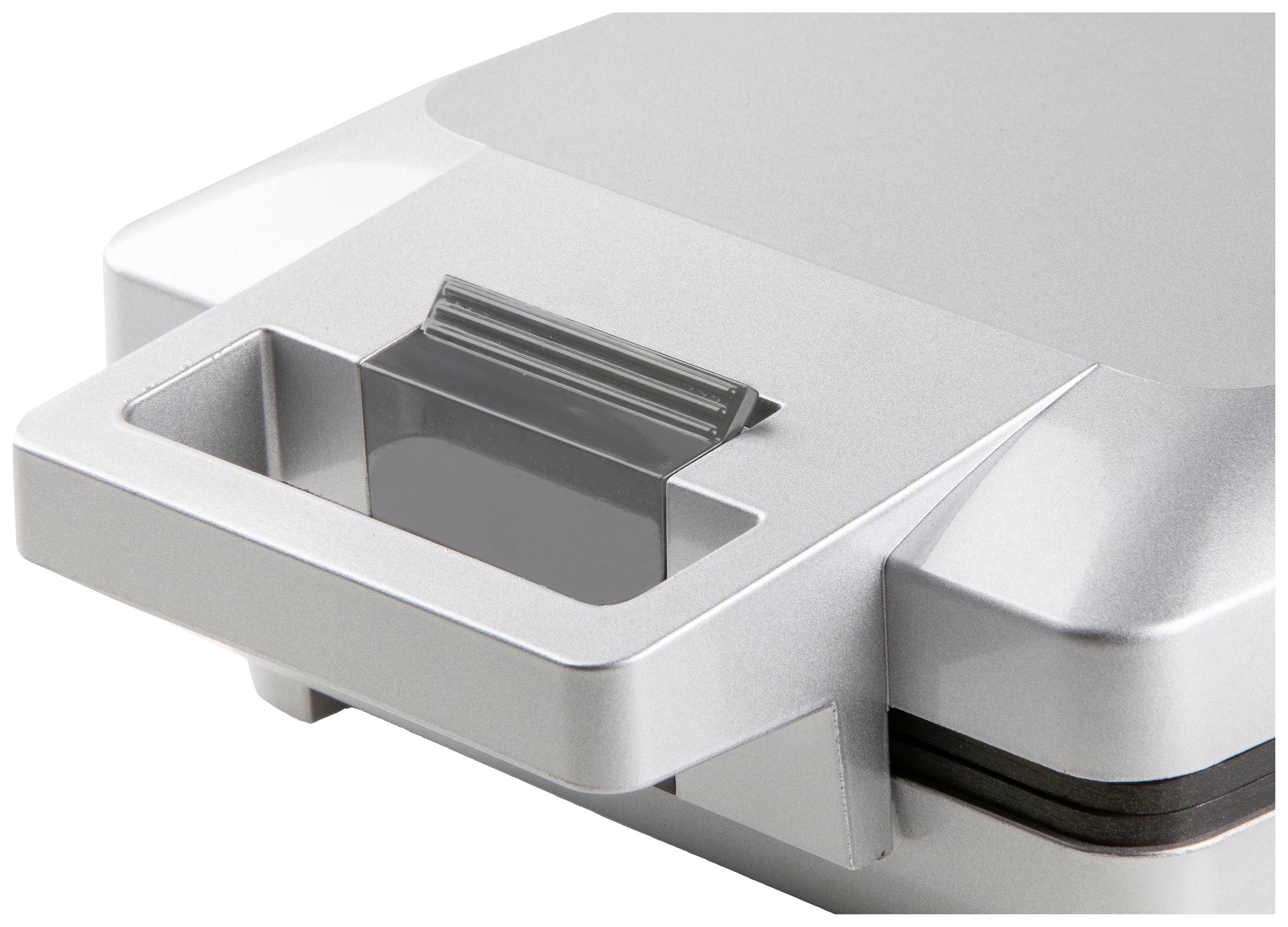 Srebrne urządzenie elektryczne o prostokątnym kształcie z uchwytem, prawdopodobnie sprzęt kuchenny taki jak toster do kanapek lub gofrownica.