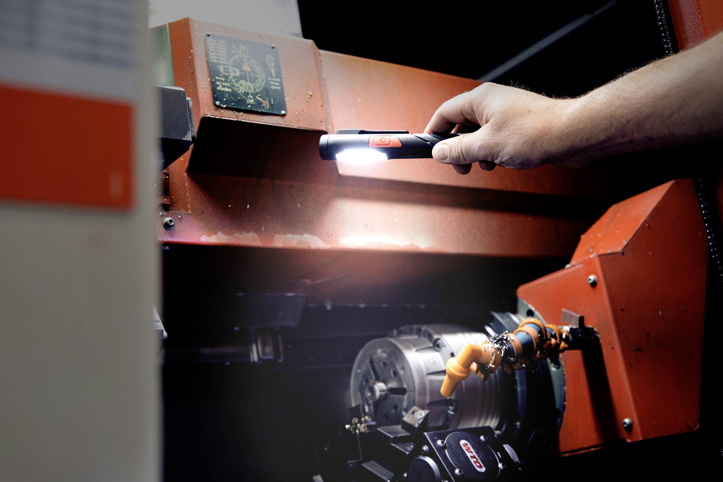 Osoba oświetla latarką fragment warsztatu maszynowego, aby sprawdzić szczegóły elementów maszyny.