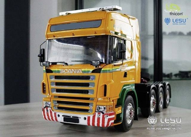 Żółta modelowa ciężarówka stoi na stole. Na kabinie kierowcy znajduje się logo producenta.