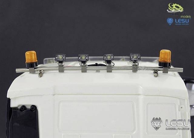 Biały model ciężarówki z pięcioma reflektorami i dwoma pomarańczowymi światłami ostrzegawczymi na dachu. Widoczne są logo marki.