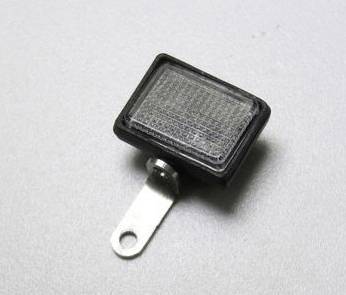 Prostokątny reflektor z tworzywa sztucznego z metalowym elementem mocującym, leżący na szarej powierzchni.