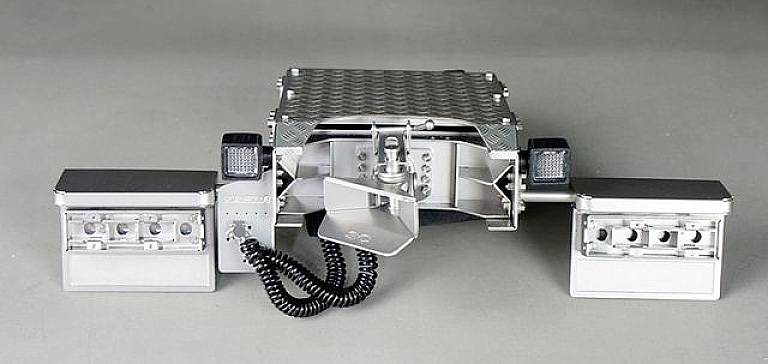 Srebrne, prostokątne urządzenie z dwoma składanymi ramionami i kablami w środowisku przemysłowym. Wygląda na sprzęt techniczny.