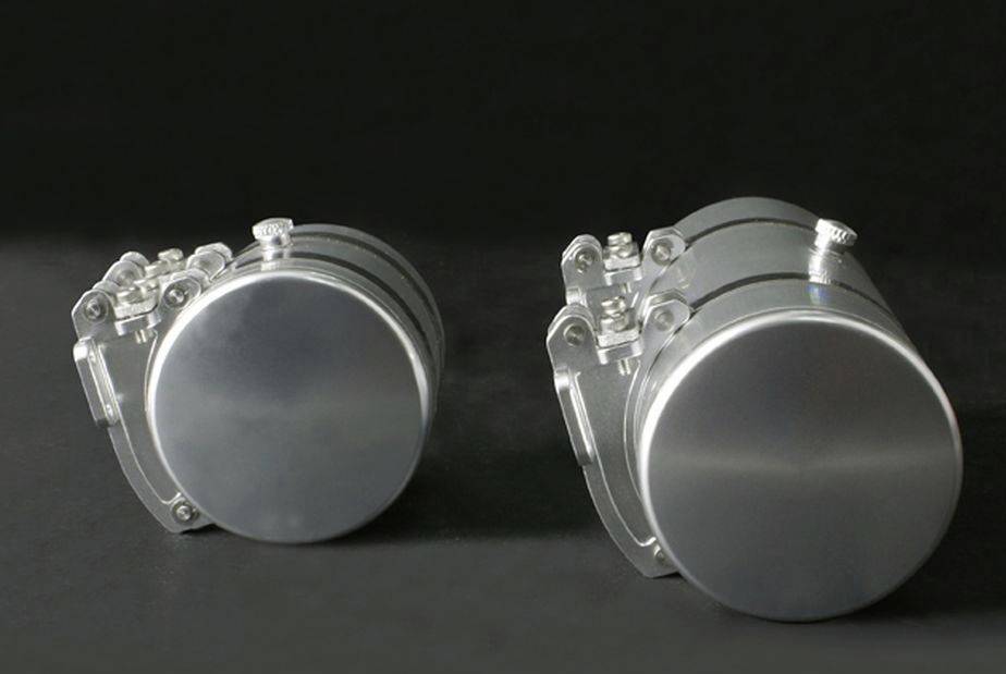 Dwa srebrzyste, cylindryczne metalowe obiekty na czarnym tle. Są umieszczone obok siebie i lekko połyskują.