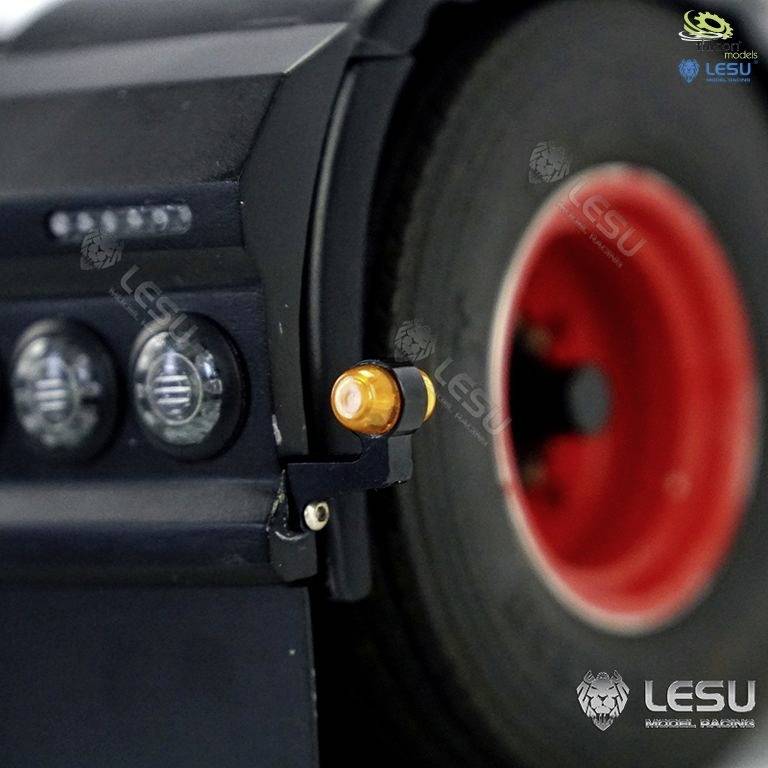 Zbliżenie koła ciężarówki z czerwonym obręczem i żółtą lampką pozycyjną. Logo LESU widoczne jest w prawym górnym rogu obrazu.