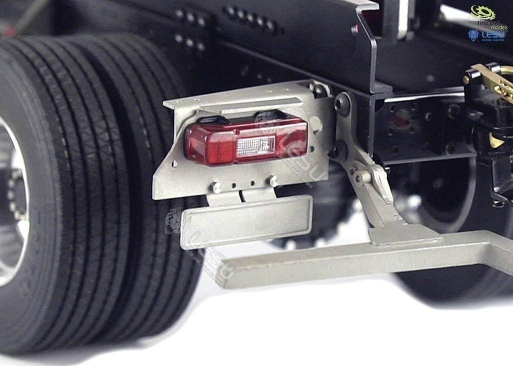 Zbliżenie tylnej lampy i uchwytu tablicy rejestracyjnej na przyczepie. Widoczne są szczegóły metalowej konstrukcji i opony.