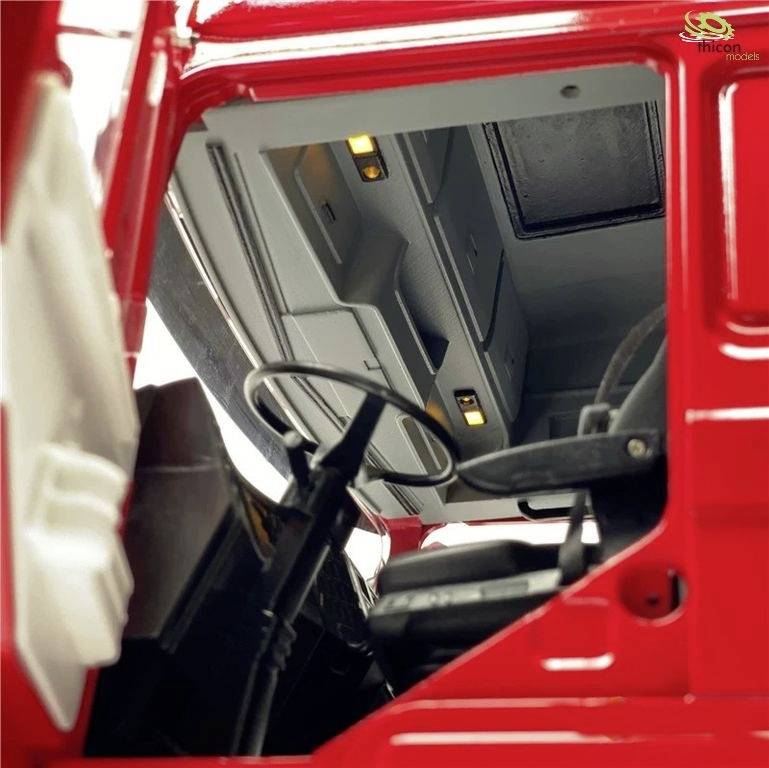 'Czerwona kabina ciężarówki z szczegółowym widokiem wnętrza, widocznym kierownicą i siedzeniami.'