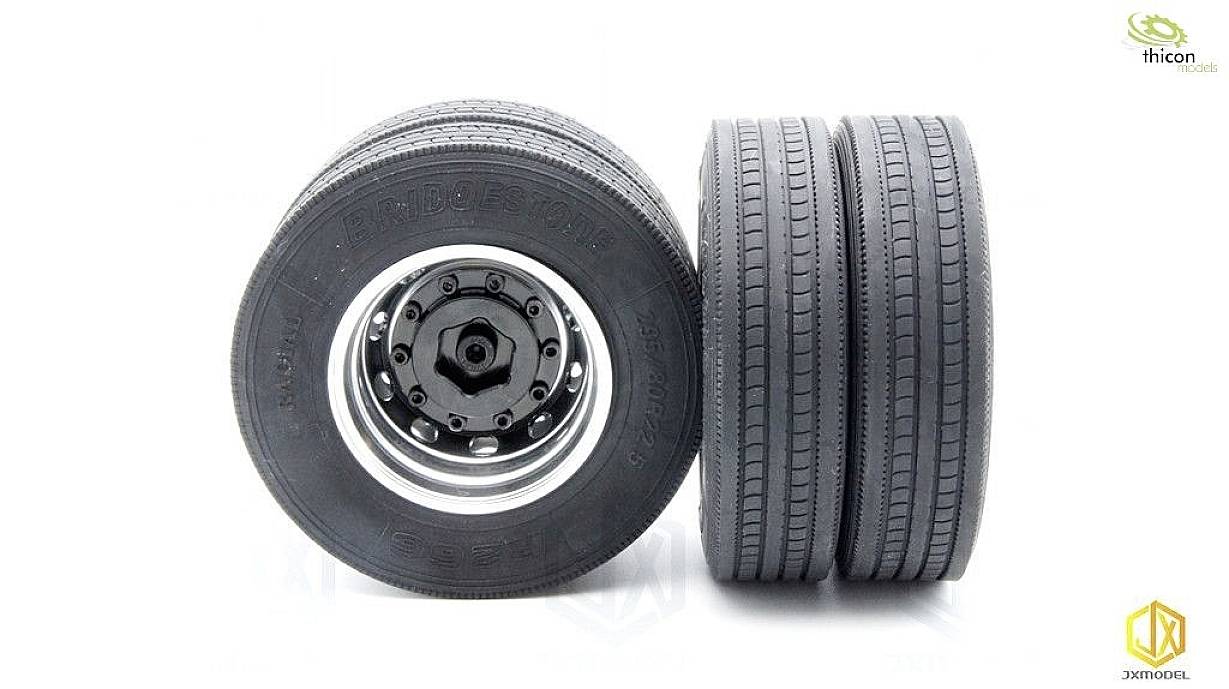 Dwa sąsiadujące ze sobą opony ciężarowe, jedna stoi pionowo, druga jest pochylona. Obie są czarne z bieżnikiem o wyrazistym wzorze.