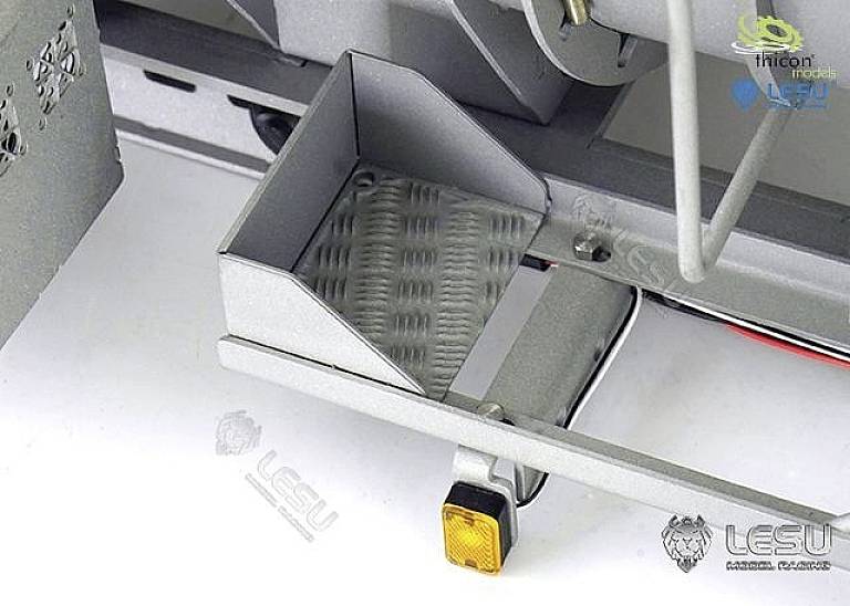 Szary element metalowy z małym wzorem siatki wewnątrz. U dołu po prawej stronie zamocowany jest mały prostokątny, żółty reflektor.