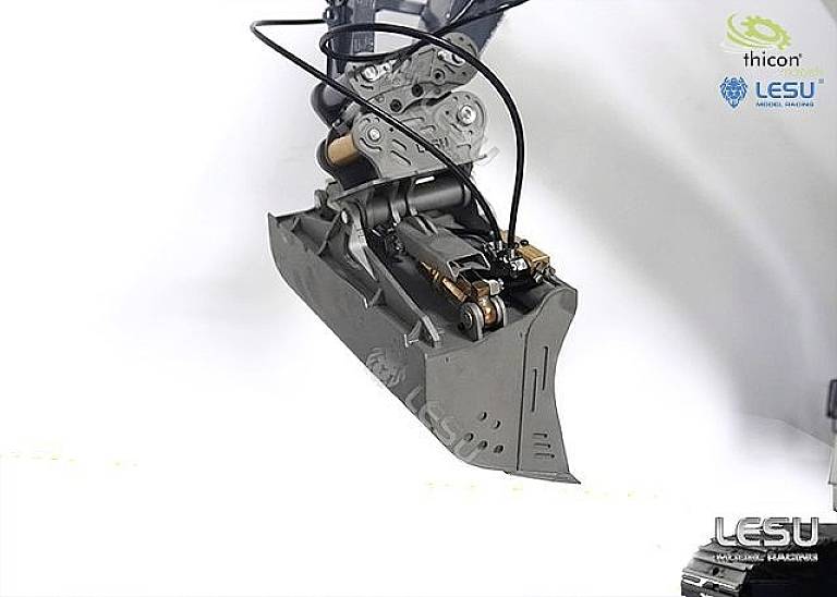 Mechaniczne ramię chwytające trzyma małą metalową łyżkę koparki. Logo firmy w górnym prawym i dolnym prawym rogu obrazu.