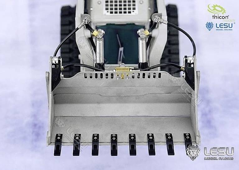 Miniaturowa koparka z uniesioną łyżką na lodowatoniebieskim tle. Logo 'Thicon' i 'LESU' widoczne są w górnym prawym rogu.