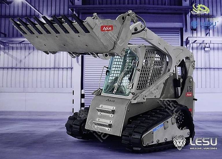 Srebrny, zdalnie sterowany ładowarka kompaktowa z gąsienicami gumowymi i podniesioną łyżką stoi w hali magazynowej.