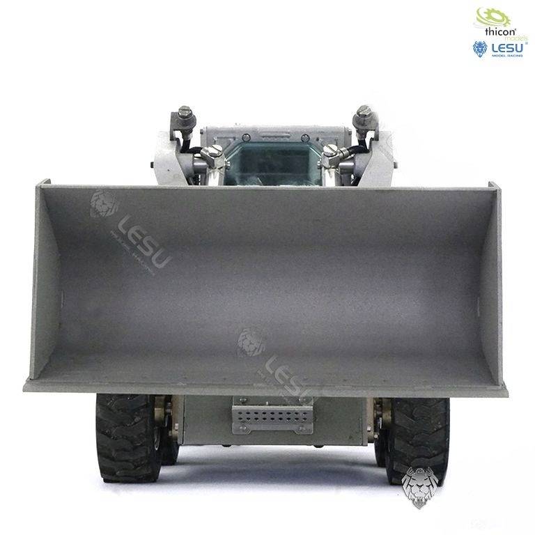 Ładowarka-koparka widziana z przodu, z dużą łyżką, solidną budową i grubą oponą bieżnikowaną na jasnym tle.