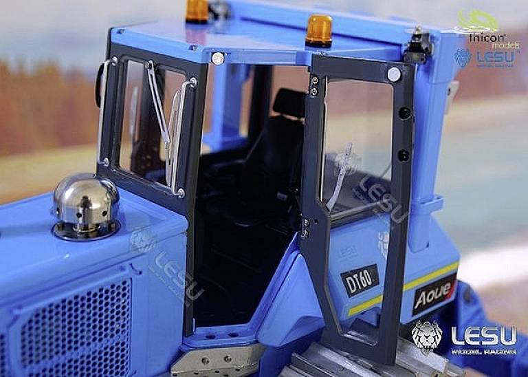 Mały model niebieskiego traktora z otwartymi drzwiami i widocznym wnętrzem, na tle przedstawiającym pole uprawne.