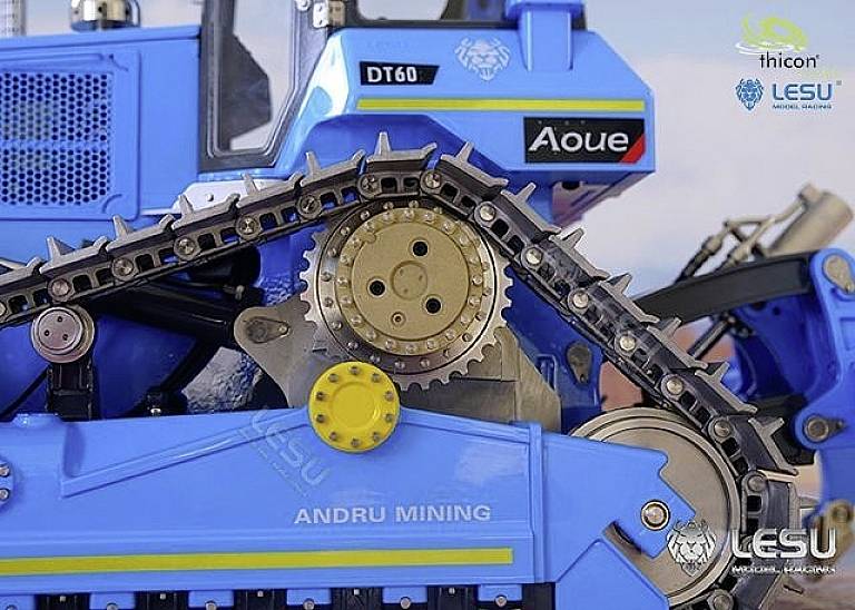Zbliżenie niebieskiego modelu pojazdu gąsienicowego z mechanizmem napędu gąsienicowego. Widoczne logo 'thicon', 'LESU' i 'ANDRU MINING'.