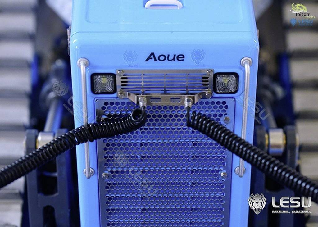 Niebieski zabawkowy samochód ciężarowy widziany z przodu, z kratką wentylacyjną i dwoma czarnymi spiralnymi kablami wystającymi z przedniej części.