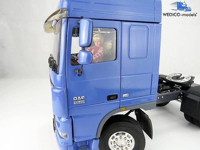 Niebieski model ciężarówki z dokładnym widokiem kabiny kierowcy. Postać siedzi za kierownicą. Tekst: 'WEDICO-models'.