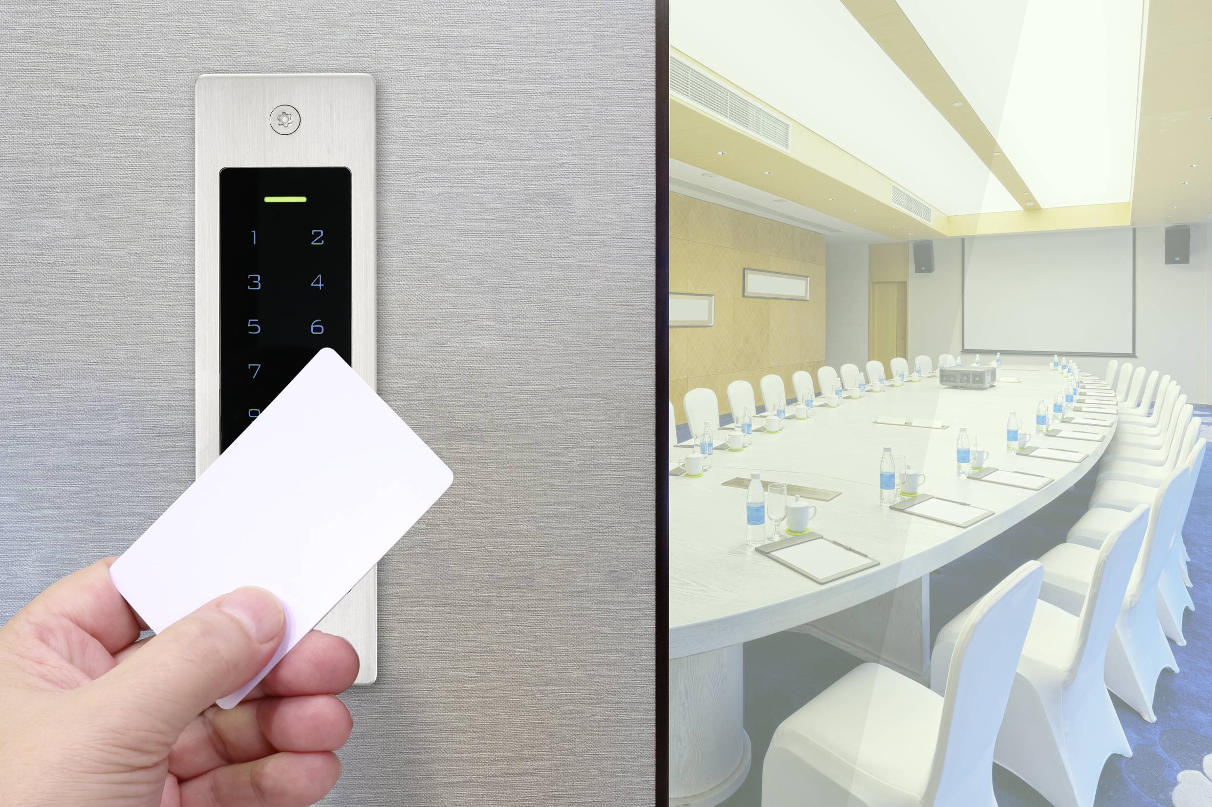 Dłoń trzyma kartę dostępową przed elektronicznym zamkiem drzwiowym, obok znajduje się sala konferencyjna z okrągłym stołem i białymi krzesłami.