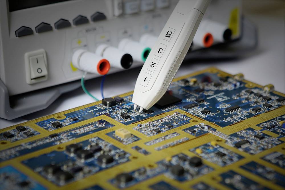 Oscyloskop z sondą pomiarową mierzy płytkę drukowaną wyposażoną w elementy elektroniczne. W tle widoczne są różne złącza.