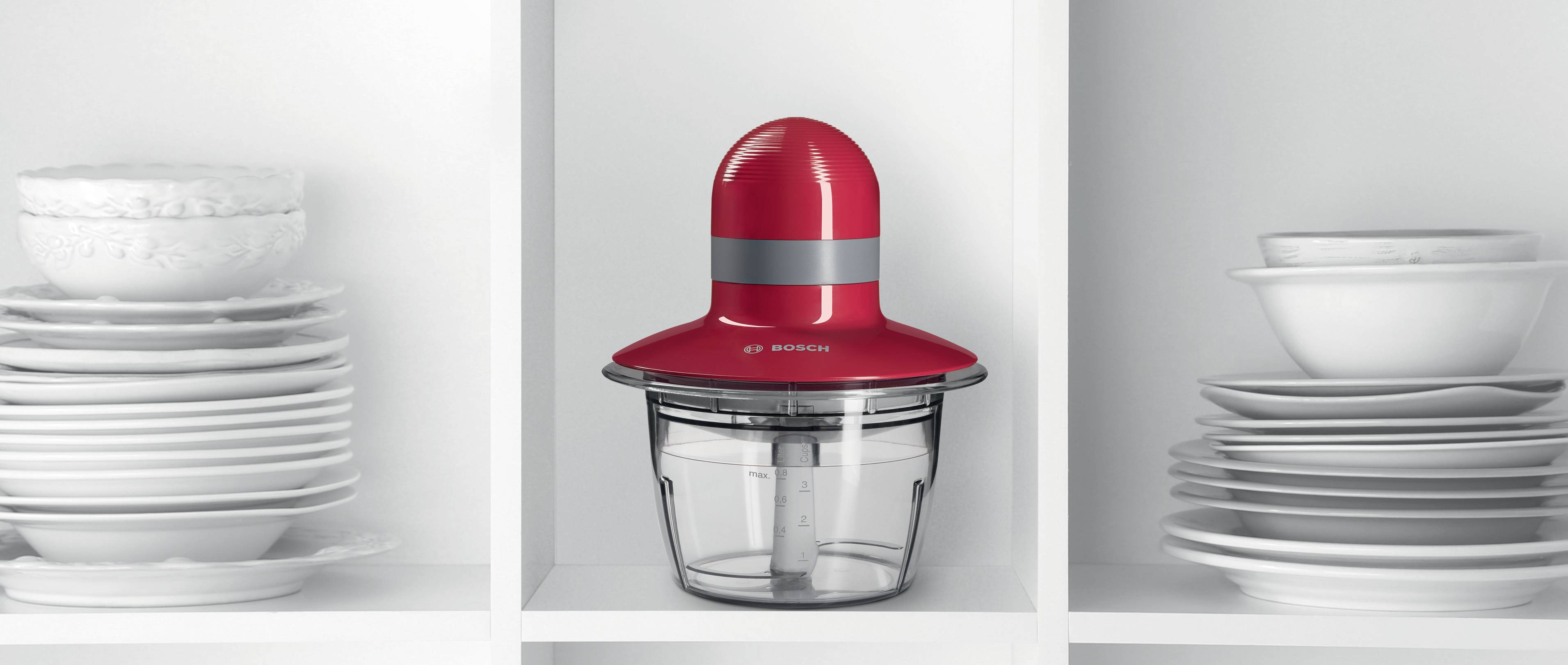 Czerwony mikser kuchenny firmy Bosch na półce, otoczony ułożonymi po obu stronach białymi talerzami.
