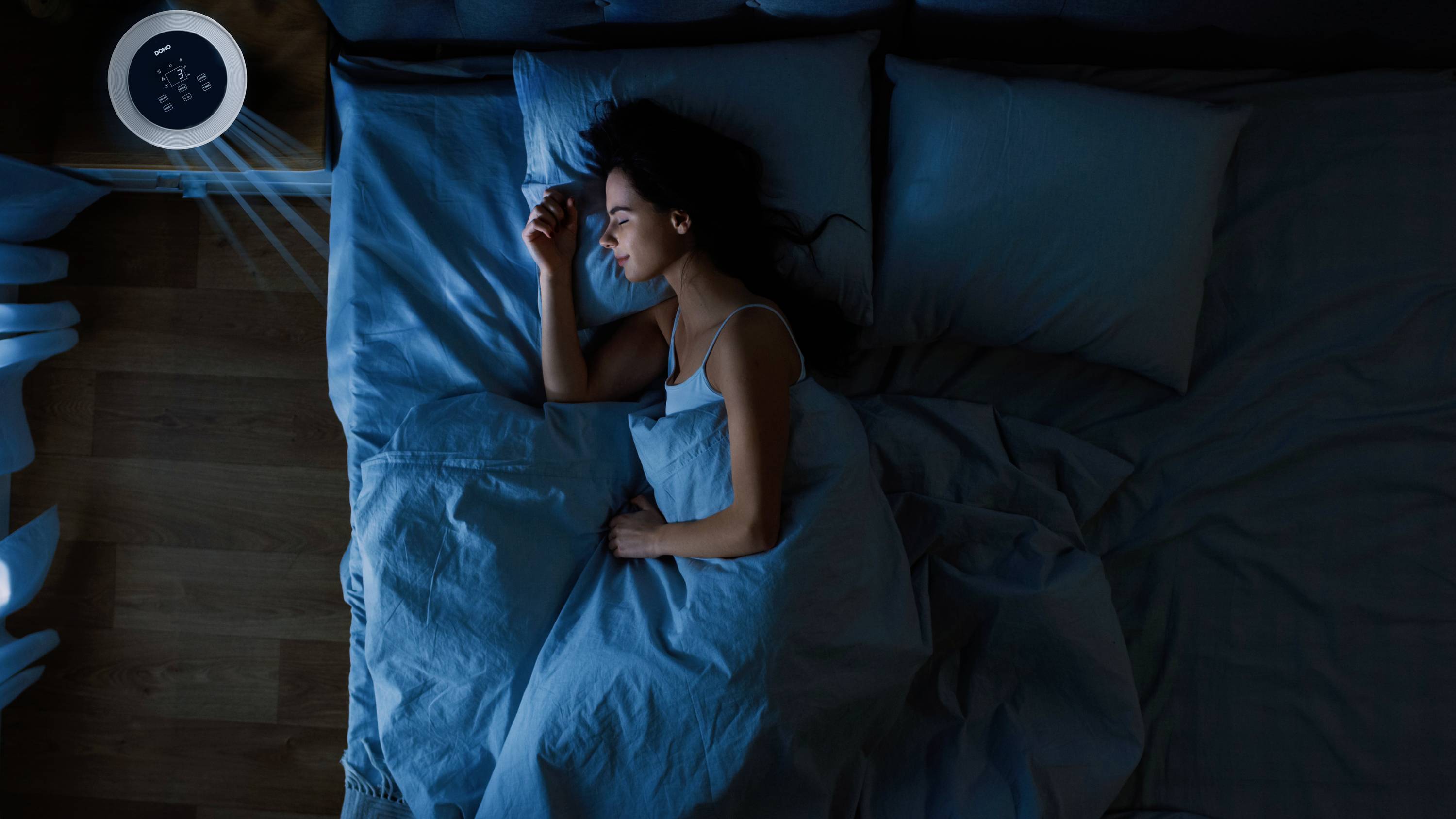 Osoba spokojnie śpi w ciemnym pokoju, podczas gdy łagodne światło nocnej lampki świeci na stoliku nocnym.