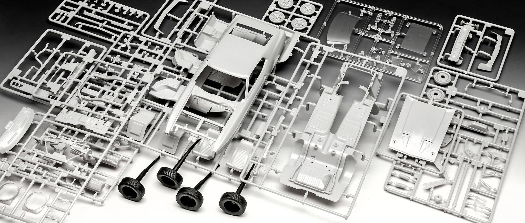 Elementy zestawu do składania modelu samochodu z tworzywa sztucznego przedstawiają nadwozie, opony i elementy wyposażenia. Części są ułożone bez określonego porządku.