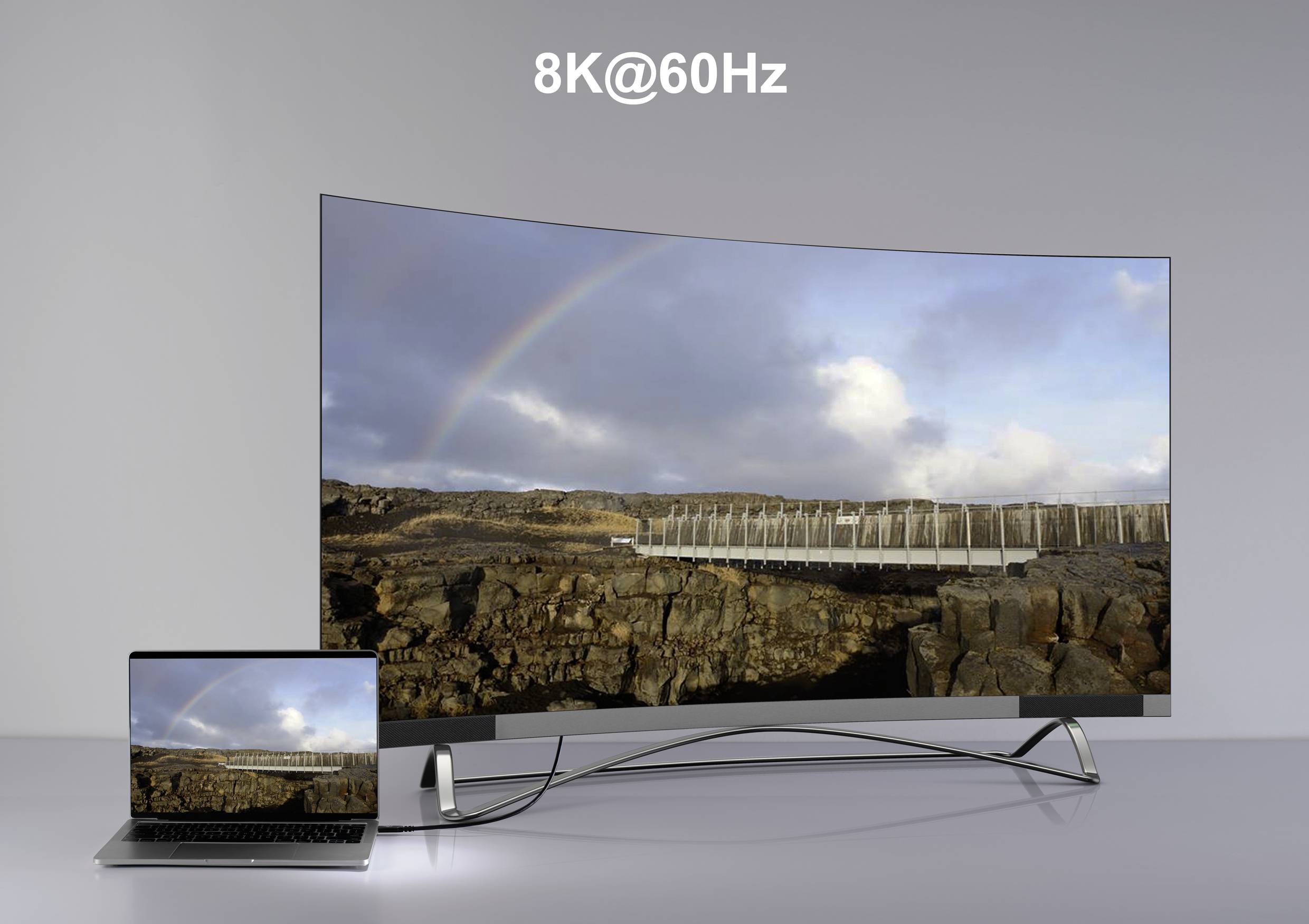 Duży zakrzywiony telewizor 8K wyświetla obraz krajobrazu z tęczą, podłączony do laptopa, który pokazuje ten sam obraz.