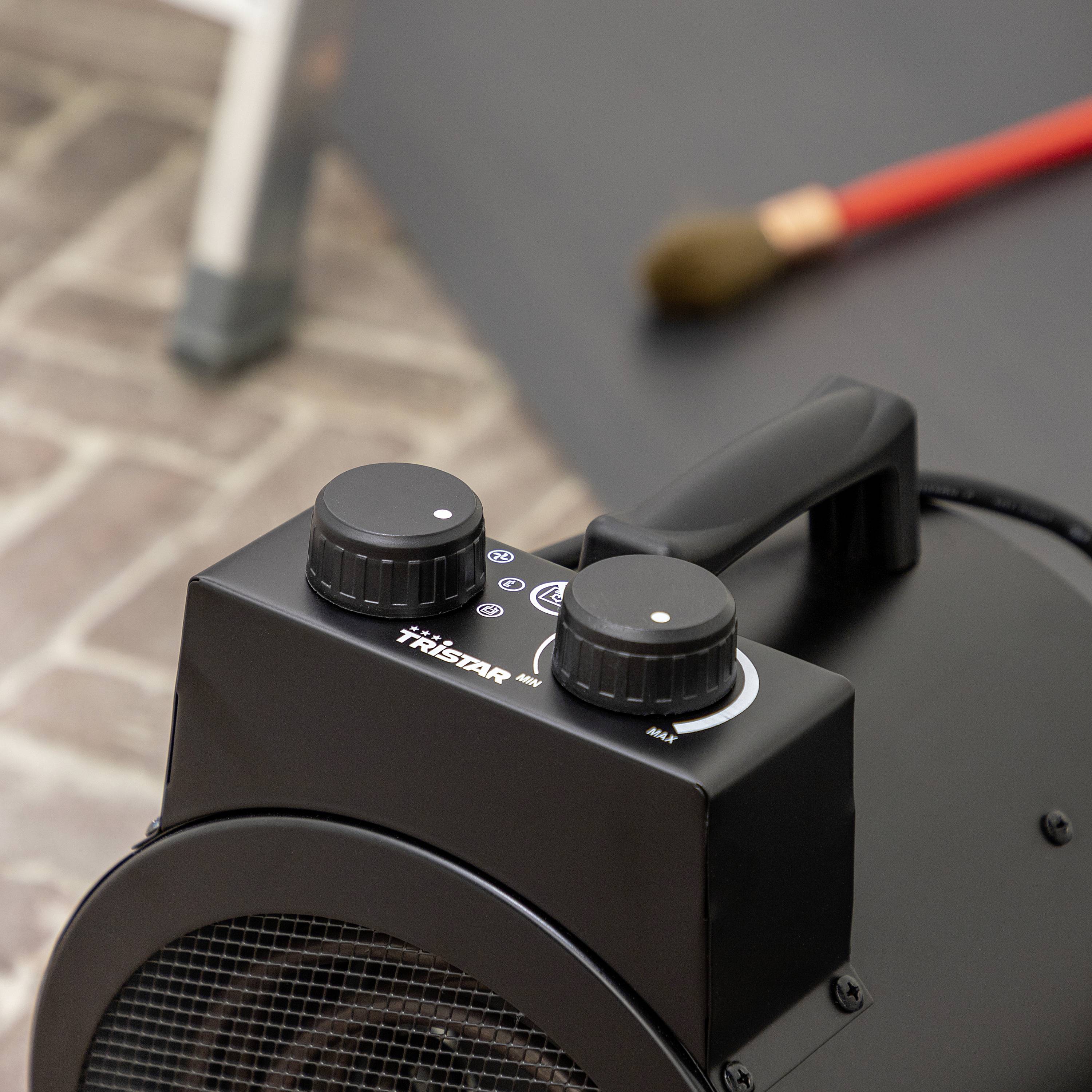 Urządzenie grzewcze stoi na powierzchni ceglastej podłogi, a w tle leży czerwona miotła. Fokus skierowany jest na element sterujący urządzenia.