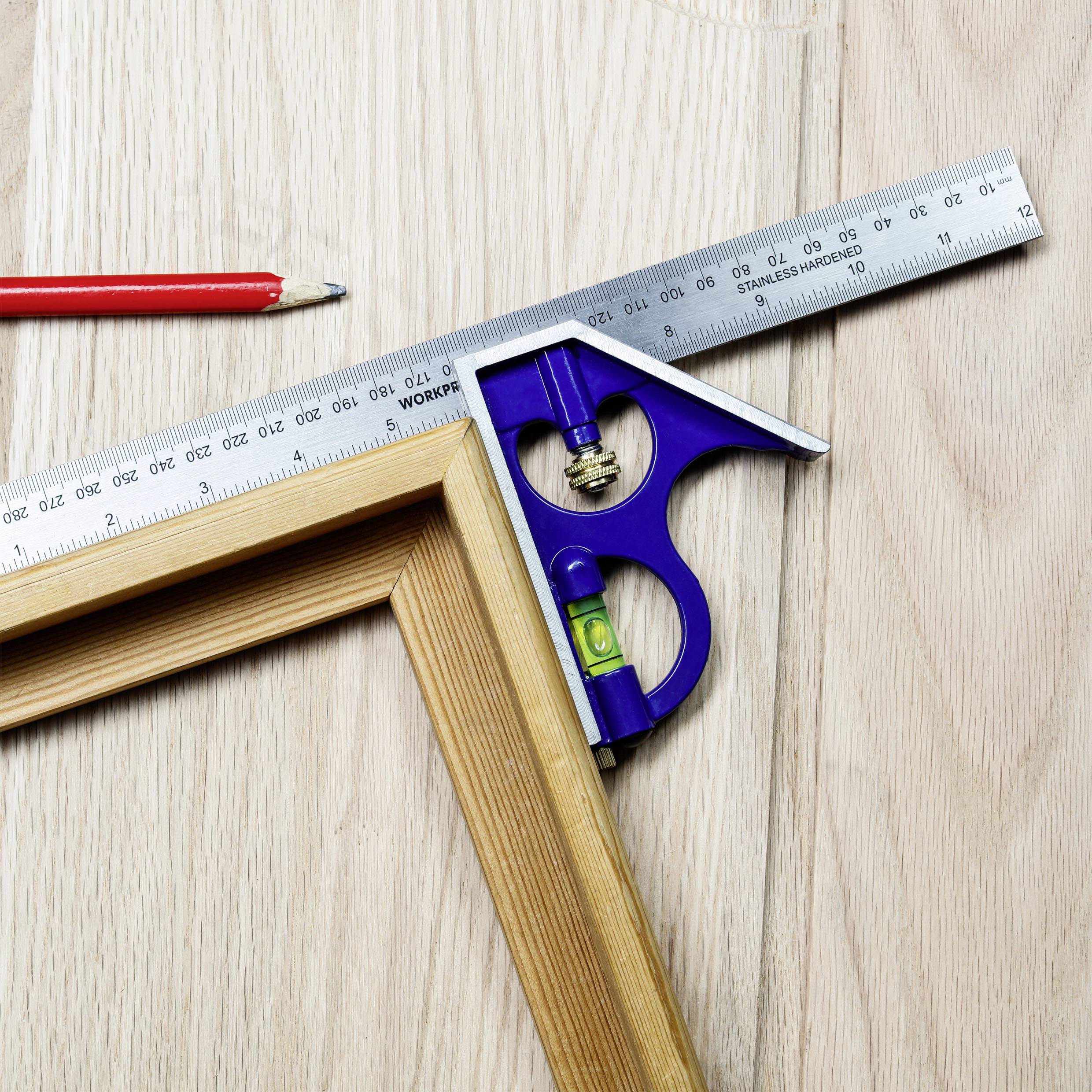 Kątownik i niebieski kątomierz z poziomicą na jasnym drewnianym stole obok czerwonego ołówka.