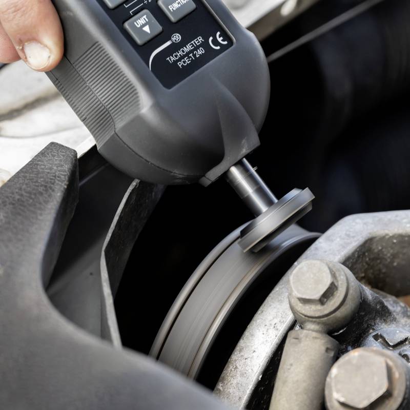 Osoba mierzy za pomocą tachometru prędkość obrotową obracającego się obiektu, prawdopodobnie części maszyny.